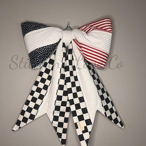 May include: A decorative bow with a variety of patterns. The bow features sections with red and white stripes, black and white checkered patterns, and navy blue polka dots. The bow is hanging against a gray background.