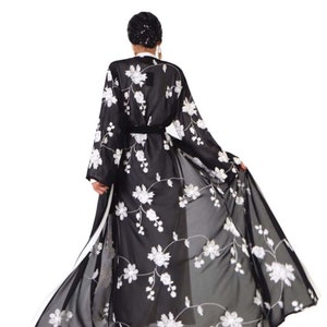May include: A black sheer robe with white floral embroidery. The robe has a long, flowing silhouette and a sash at the waist.