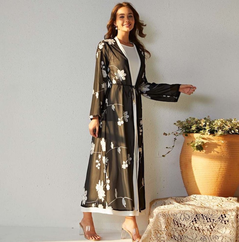 May include: A long black sheer cardigan with white floral embroidery. The cardigan has a tie at the waist and long sleeves.
