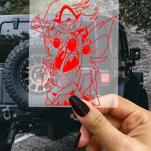 May include: A red cartoon character sticker with a wide grin and multiple eyes is held in front of a black Jeep. The sticker features a detailed design with sharp lines and a transparent background. The text "AQUARIAN MOON DESIGN" is visible.