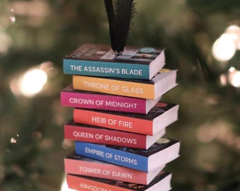 May include: A miniature book stack ornament featuring titles from the Throne of Glass series including The Assassin's Blade, Throne of Glass, Crown of Midnight, Heir of Fire, Queen of Shadows, Empire of Storms, Tower of Dawn, and Kingdom of Ash.