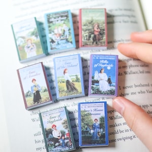 Könnte beinhalten: Eine Sammlung von Miniaturbüchern mit farbenfrohen Einbänden, darunter Titel wie "Anne of Ingleside" und "Rilla of Ingleside". Die Bücher werden auf einem offenen Buch präsentiert, mit Illustrationen von Personen und Landschaften auf den Einbänden.