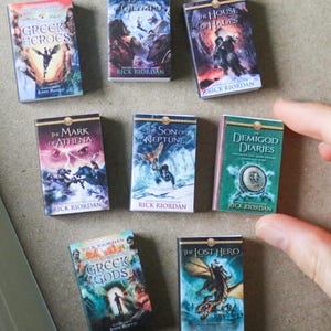 May include: Miniature book set featuring titles like "Greek Heroes," "The Blood of Olympus," and "The House of Hades." Each book has a colorful cover with fantasy art and the author's name, Rick Riordan.