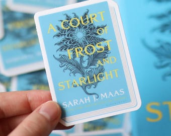 Op de afbeelding: Een blauwe en witte sticker met de tekst "A Court of Frost and Starlight" van Sarah J. Maas. De sticker heeft een gestileerd bloemmotief.