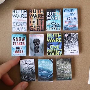 May include: A white ceramic mug with a black handle and the text "But First, Coffee" in a bold, black font. The mug is set against a blurred background, suggesting a cosy setting.