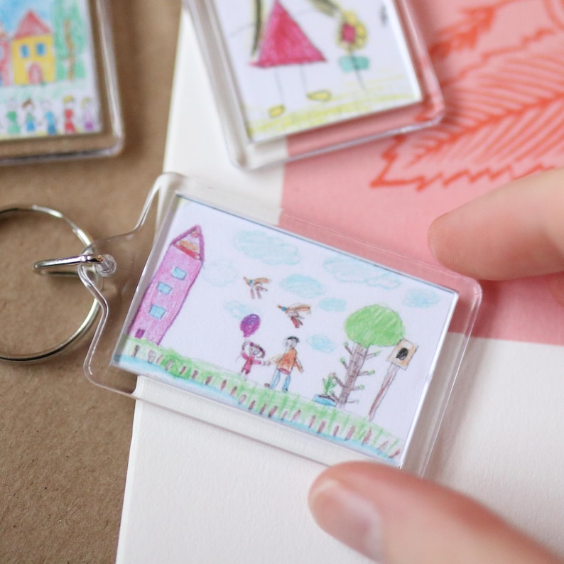 Peut inclure: Un porte-cl&eacute;s en plastique transparent avec un dessin color&eacute; d'une famille, d'une maison et d'un arbre. Le dessin est prot&eacute;g&eacute; par un couvercle en plastique transparent.