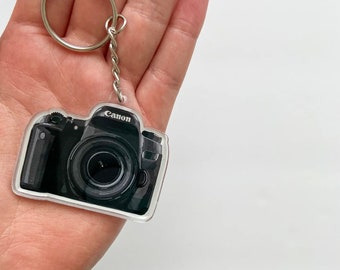 May include: A black and silver camera keychain with the word "Canon" printed on it.