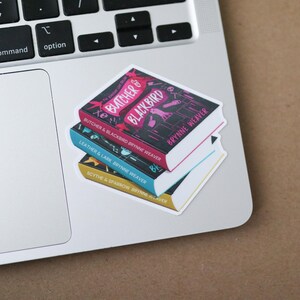 Pu&ograve; includere: Una pila di tre adesivi per libri su un laptop. L'adesivo superiore &egrave; nero con testo rosa "Butcher & Blackbird". Quello centrale &egrave; blu con "Leather & Lark". Quello inferiore &egrave; dorato con "Scythe & Sparrow".
