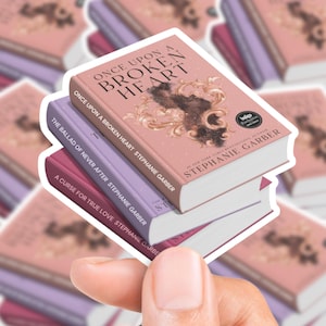 Pode incluir: Uma pilha de três livros com os títulos "Once Upon a Broken Heart", "The Ballad of Never After" e "A Curse for True Love" de Stephanie Garber. O livro de cima é rosa com detalhes dourados.