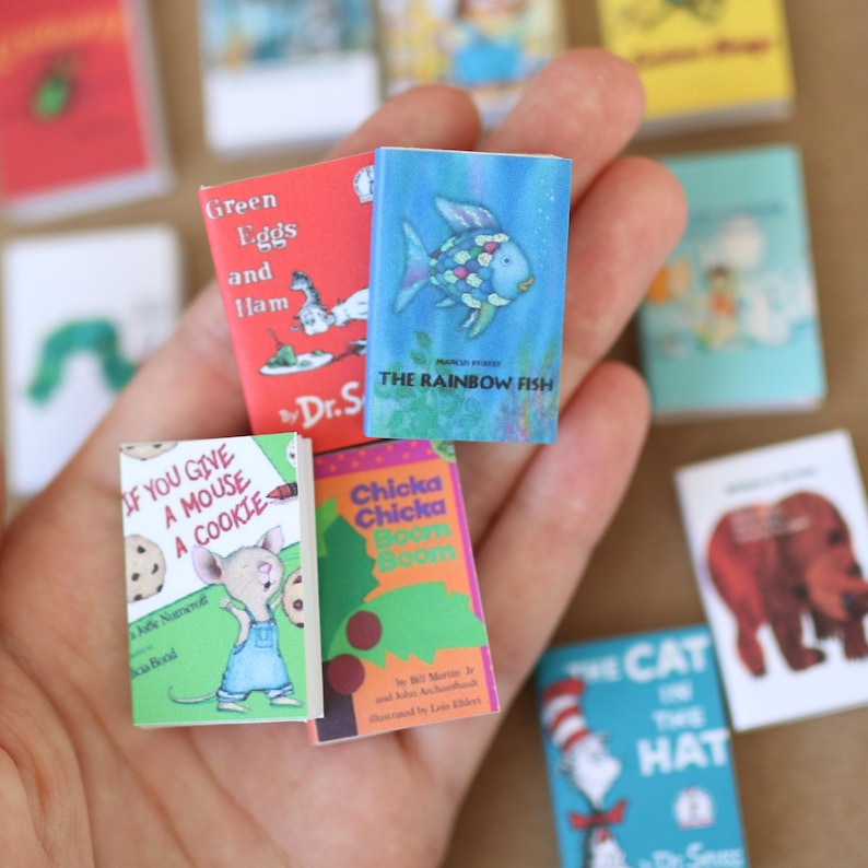 May include: A collection of miniature children's books, including "Green Eggs and Ham," "The Rainbow Fish," and "If You Give a Mouse a Cookie." The books have colorful covers and are held in a hand.