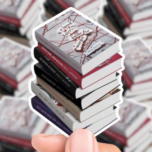 以下が含まれることがあります： 「A Good Girl's Guide to Murder」や「Five Survive」など、Holly Jacksonの7冊の本のスタック。本は、赤、黒、白など、さまざまな色の背表紙があり、表紙にはテキストが見えます。
