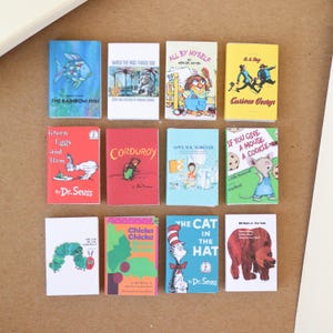 May include: A collection of miniature children's books with colorful covers. Titles include "The Rainbow Fish," "Curious George," and "The Cat in the Hat." The books are arranged on a neutral surface.