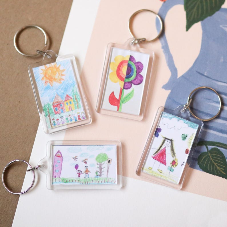Peut inclure: Quatre porte-cl&eacute;s en plastique transparent avec des dessins color&eacute;s &agrave; l'int&eacute;rieur. Les dessins comprennent une maison avec un soleil, une fleur, une famille avec un ballon et une fille tenant une fleur.