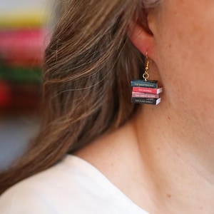 Puede incluir: Pendientes colgantes dorados con forma de pilas de libros en miniatura. Cada libro tiene un lomo de diferente color y t&iacute;tulo: "The Nightingale", "The Women", "The Great Alone" y "The Four Winds". Un accesorio original para amantes de los libros.