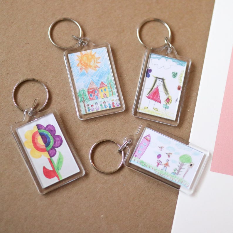 Peut inclure: Quatre porte-cl&eacute;s en plastique transparent avec des dessins color&eacute;s &agrave; l'int&eacute;rieur. Les dessins comprennent une maison avec un soleil, une fille en robe rouge, une fleur et une maison avec une famille.