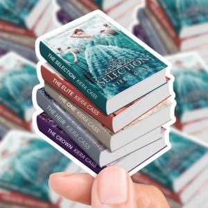 Könnte beinhalten: Ein Stapel von fünf Büchern aus der "Selection"-Reihe von Kiera Cass. Das oberste Buch hat einen türkisfarbenen Einband mit einer Frau in einem Kleid. Die anderen Bücher haben rote, graue und violette Einbände. Die Titel lauten "The Selection", "The Elite", "The One", "The Heir" und "The Crown".