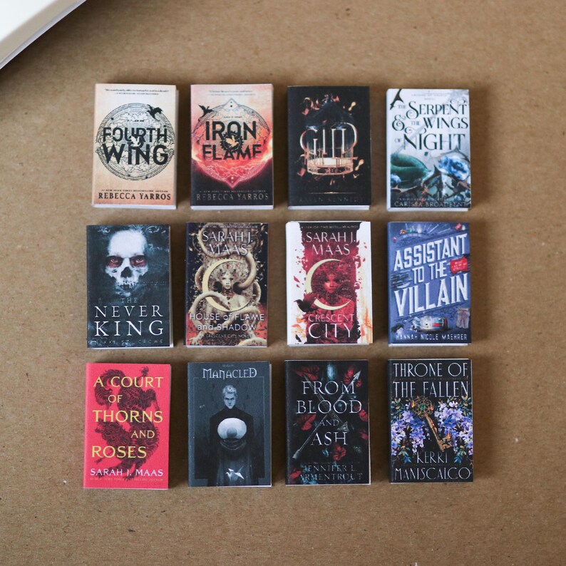 Op de afbeelding: Een verzameling miniatuur fantasy romans met kleurrijke covers. Titels zijn onder meer "Fourth Wing", "Iron Flame", "Serpent & the Wings of Night" en "A Court of Thorns and Roses". De boeken zijn gerangschikt op een neutrale ondergrond.
