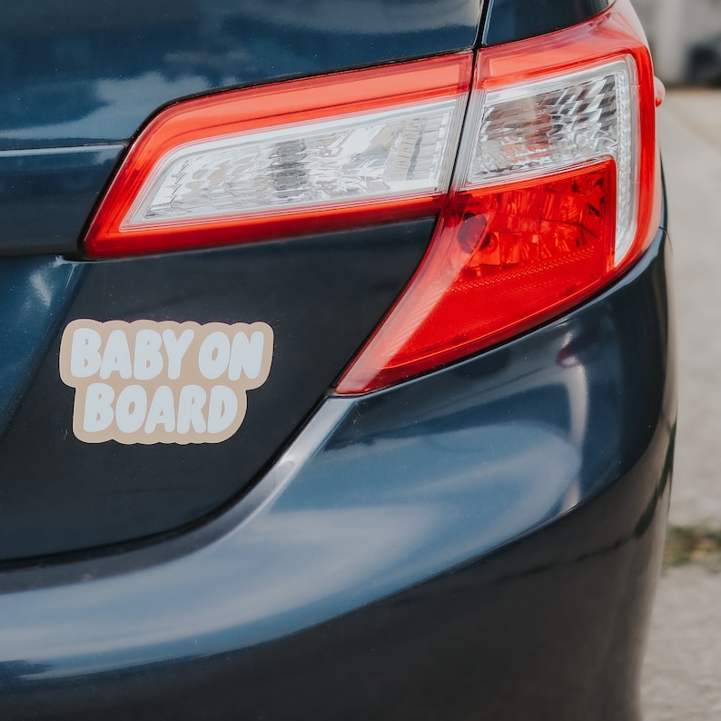 May include: A blue car with a "Baby On Board" sticker on the back bumper. The sticker is tan with white lettering.