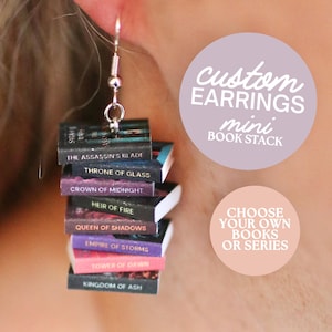 May include: A silver earring with a stack of miniature books. Each book has a different title, including "The Assassin's Blade" and "Kingdom of Ash." The text on the image reads "custom earrings mini book stack" and "choose your own books or series."
