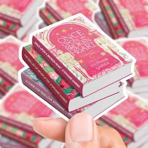 May include: A stack of three stickers depicting book covers. The top sticker is pink and features the title "Once Upon a Broken Heart" and the author's name. The middle sticker is red with the title "The Ballad of Never After". The bottom sticker is purple with the title "A Curse for True Love".