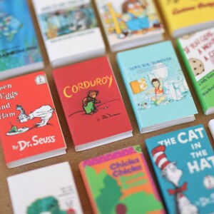 May include: A collection of miniature children's books with colorful covers. Titles include "Corduroy", "The Cat in the Hat", and "Green Eggs and Ham" by Dr. Seuss. The books are arranged closely together, showcasing various illustrations and text.