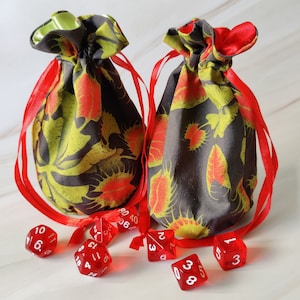 May include: Two black and green fabric bags with red ribbon ties and red dice with white numbers. The bags have a floral pattern with red and yellow accents.