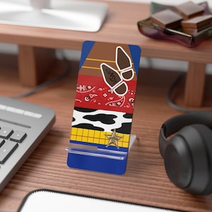 Puede incluir: Un soporte para teléfono azul, rojo, amarillo y blanco con una huella de bota de vaquero y una estrella de sheriff. El soporte está hecho de plástico y tiene un soporte de plástico transparente para un teléfono.