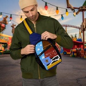 Puede incluir: Un bolso bandolera con un dise&ntilde;o de patchwork que incluye un cielo azul con nubes blancas, una secci&oacute;n marr&oacute;n, un patr&oacute;n de bandana roja, un estampado de vaca en blanco y negro, una estrella dorada sobre un cuadrado azul y una cuadr&iacute;cula amarilla y naranja.