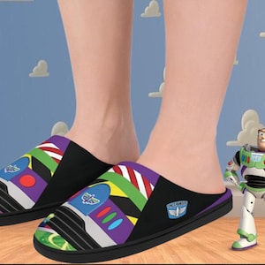 Puede incluir: Un par de zapatillas negras y coloridas con temática de Toy Story. Las zapatillas presentan un diseño de la nave espacial de Buzz Lightyear con el texto "Space Ranger" en el lateral. Las zapatillas las lleva puestas una persona de pie sobre un suelo de madera.