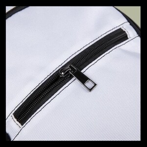 Puede incluir: Una superficie de tela blanca con un cierre de cremallera negro y un tirador met&aacute;lico rectangular. La cremallera est&aacute; integrada en un borde negro con costuras visibles, creando un contraste n&iacute;tido con el material blanco texturizado del bolso.