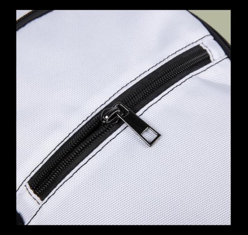 Puede incluir: Una superficie de tela blanca con un cierre de cremallera negro y un tirador met&aacute;lico rectangular. La cremallera est&aacute; integrada en un borde negro con costuras visibles, creando un contraste n&iacute;tido con el material blanco texturizado del bolso.