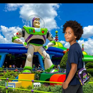 Puede incluir: Una persona joven con una camisa negra y una bolsa de bandolera morada y verde se encuentra frente a una gran estatua de Buzz Lightyear verde y morada en un parque de atracciones. La estatua est&aacute; sobre una plataforma con una base amarilla, verde y roja.