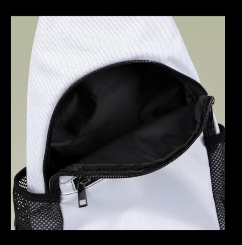 Puede incluir: Una mochila bandolera blanca con un compartimento frontal grande y abierto con forro interior negro. La bolsa incluye un cierre de cremallera negro y bolsillos laterales de malla negra a ambos lados, mostrando el espacio de almacenamiento.