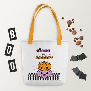 Op de afbeelding: Witte tote bag met oranje handvatten. De tas heeft een zwart-wit geruit patroon aan de onderkant en een afbeelding van twee schattige pompoenen met de tekst "Cute but Spooky" erboven.