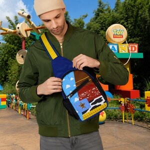 Puede incluir: Un bolso bandolera con un dise&ntilde;o de patchwork inspirado en Woody de Toy Story. El bolso incluye un patr&oacute;n de cielo azul con nubes, un estampado de bandana roja, un estampado de vaca, un borde de cuadros amarillos y un emblema de estrella dorada.