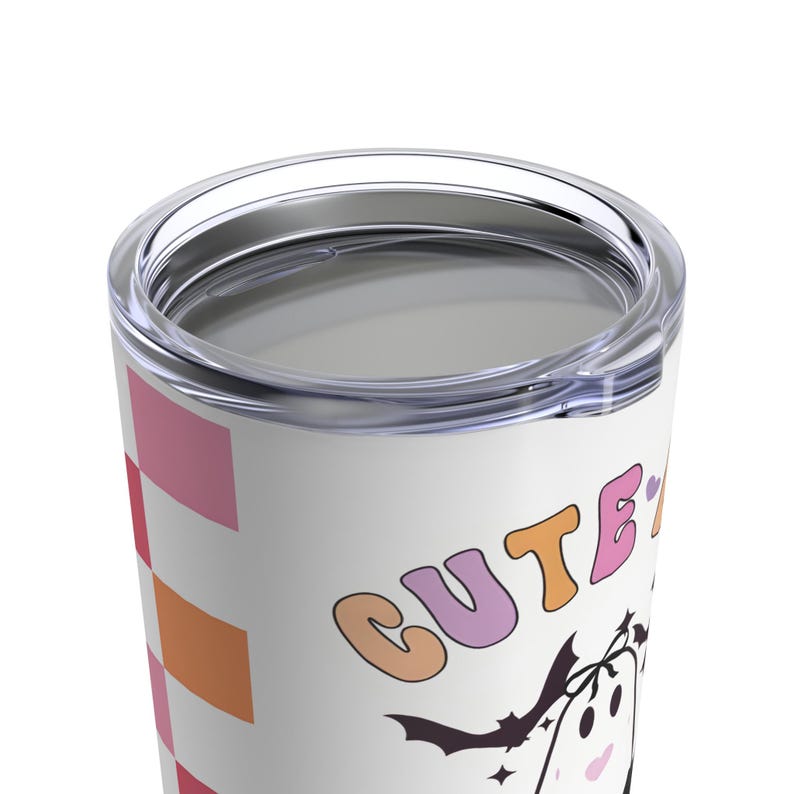 K&ouml;nnte beinhalten: Ein wei&szlig;er Edelstahlbecher mit einem pinkfarbenen, orangen und roten Karomuster. Der Becher tr&auml;gt den Text "CUTE" in Regenbogenfarben und ein Cartoon-Gespenst mit Fledermausfl&uuml;geln.