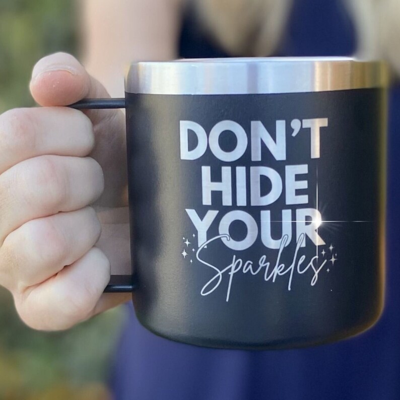 May include: Black stainless steel travel mug with a white inscription that reads "Don't Hide Your Sparkles".