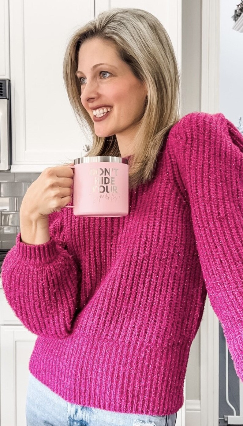 May include: A woman wearing a pink sweater with glitter holds a pink travel mug with the text "Don't Hide Your Sparkle".