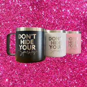 May include: Three stainless steel travel mugs with a silver lid and handle. The mugs are black, white, and pink. Each mug has the text "Don't Hide Your Sparkles" printed on the front in a gold metallic font.