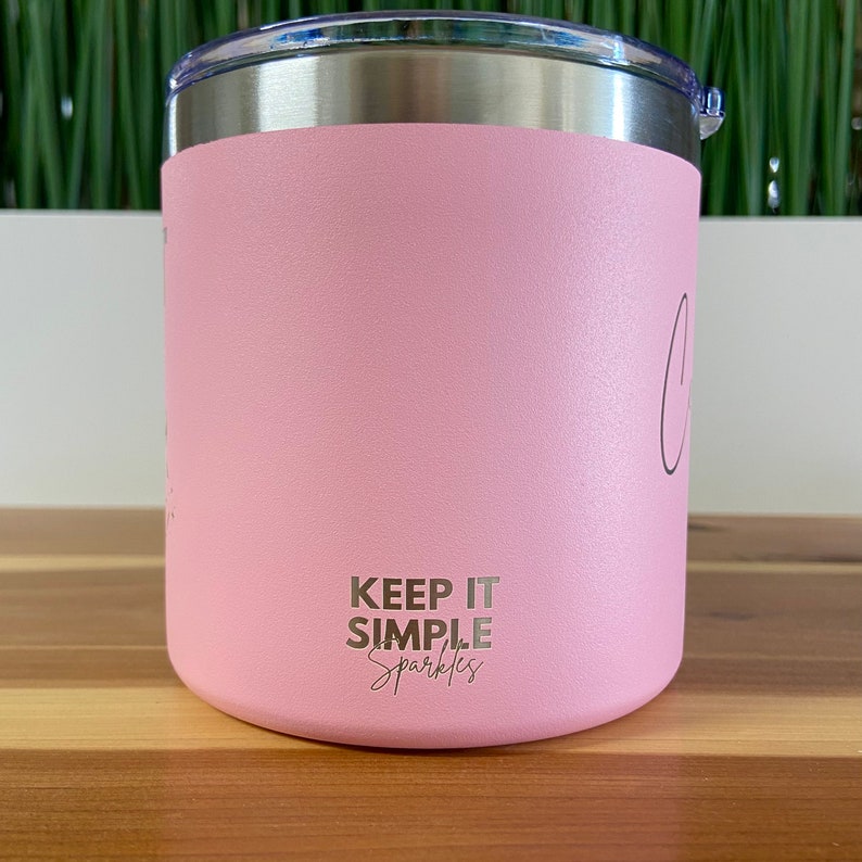 May include: A pink stainless steel tumbler with a silver lid. The tumbler has the text "Keep it simple sparkles" printed on the bottom.