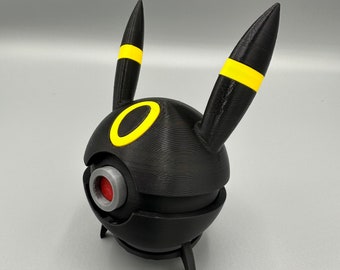 May include: Black and yellow 3D printed figurine of a Pokemon character. The character has a round body with a red eye and two pointed ears with yellow stripes.