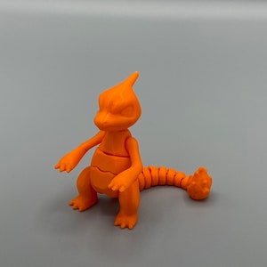 May include: Orange articulated plastic toy figure of a Pokemon character. The figure is sitting with its tail curled around its body.