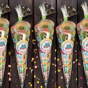 May include: Six clear plastic cones filled with colourful sweets and topped with a sticker that says "Birthday Party". The cones are arranged in a row on a wooden surface.