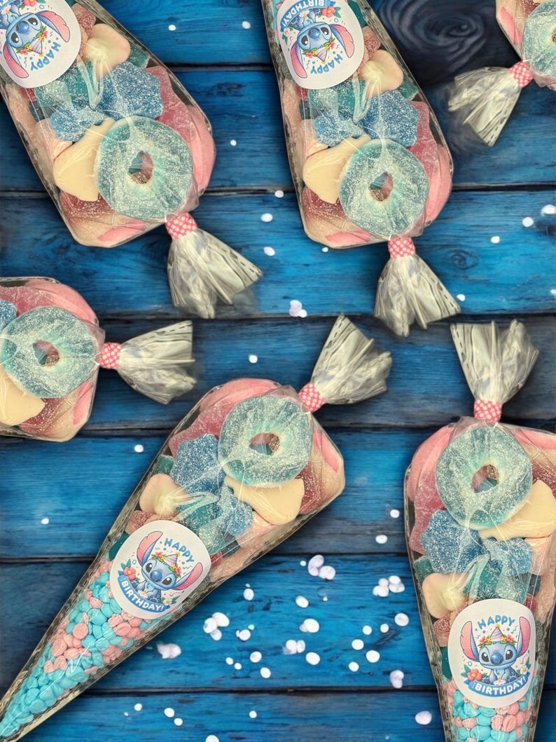 May include: Several clear cellophane bags filled with colorful candies, including blue, pink, and yellow sweets. Each bag is tied with a pink and white ribbon and features a sticker with a cartoon character and the words "Happy Birthday".