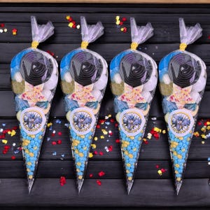 May include: Four transparent cone-shaped bags filled with sweets. Each bag has a Batman logo sticker and the text "Gotham Saves the Day". The sweets include blue and yellow candies, black licorice, and star-shaped sweets, tied with a gold ribbon.
