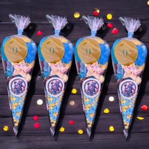 May include: Four cellophane cone bags filled with sweets. Each bag has a Superman logo sticker and is tied with a blue and white ribbon. The sweets include yellow and blue candies, star-shaped sweets, and a large yellow candy roll. The text on the sticker reads "SUPERMAN SAVES THE DAY".