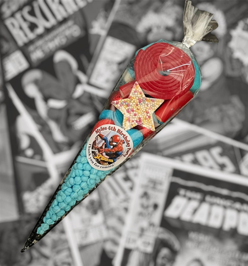May include: A cellophane cone filled with blue sweets, red liquorice, and a star-shaped sweet. A round sticker with Spider-Man is on the cone. The text on the sticker reads "Myle's 4th Birthday Party. Thank you for coming!"