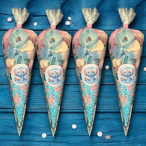 May include: Four candy cones filled with a variety of sweets, including blue and pink candies, gummy rings, and other colorful treats. Each cone has a sticker with a cartoon character and the words "Happy Birthday". The cones are tied with a pink ribbon.