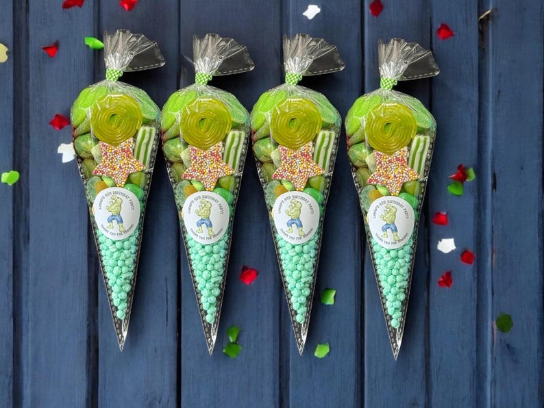 May include: Four transparent cone-shaped bags filled with green sweets, including gummy rings, star-shaped sprinkles, and round mints. Each bag has a circular sticker with a cartoon character and the text "Happy 4th Birthday Party". The bags are tied with a silver twist tie.