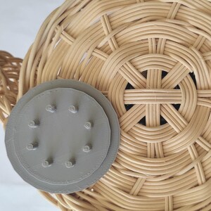 May include: A light brown woven basket with a circular pattern. A grey, circular lid with small pegs is placed on the side. The basket's intricate weave creates a textured surface. The basket is suitable for storage or display.